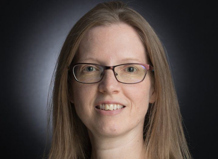 A headshot of a woman with dark hair and glasses against a black background. She is Dr Róisín Dwyer.