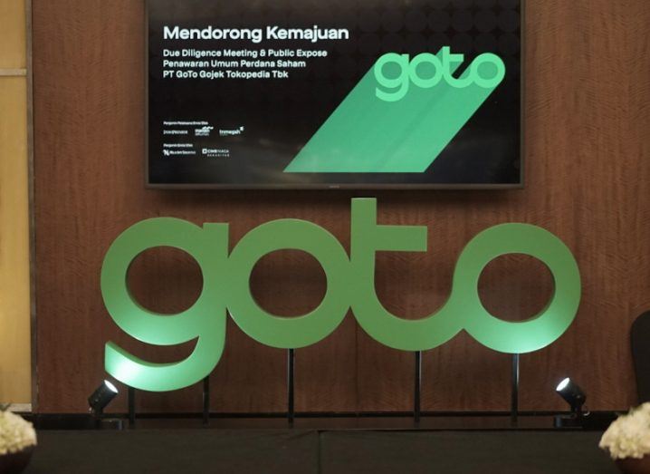 Green GoTo logo and above it a screen with some text and another GoTo logo all in front of a wooden-panelled wall.