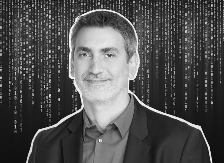 A black and white image of a man in a suit in front of a background of binary code. He is the CTO of Rapid7.