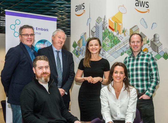 A group of men and women stand in front of posters, one of which has the AWS logo on it.