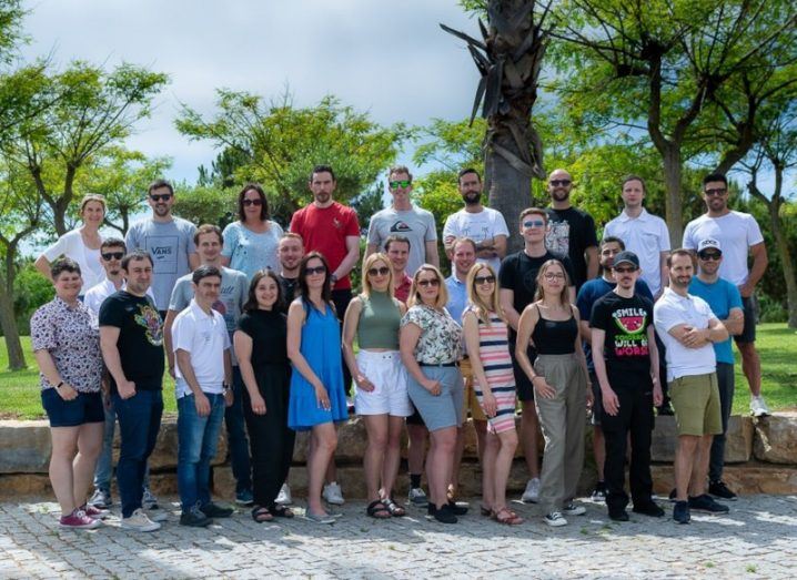 Snigel team photo - A group of approximately 25 people all dressed in summer clothes standing outside in front of palm trees and a blue sky.