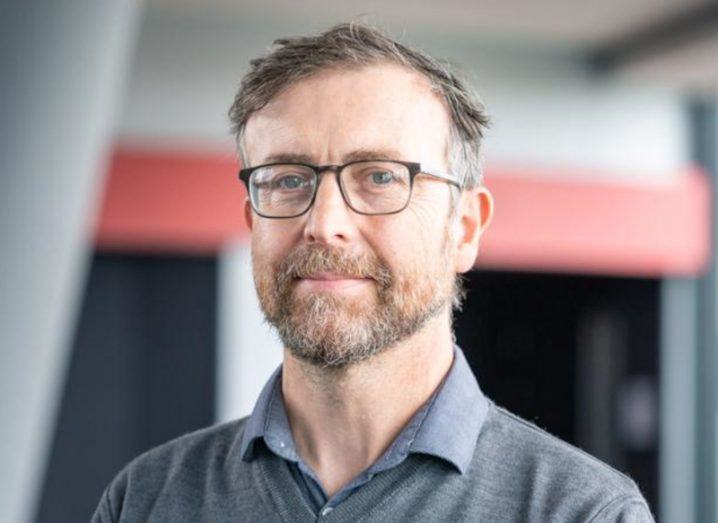 Tomás Ward wearing a grey jumper with a building wall in the background.