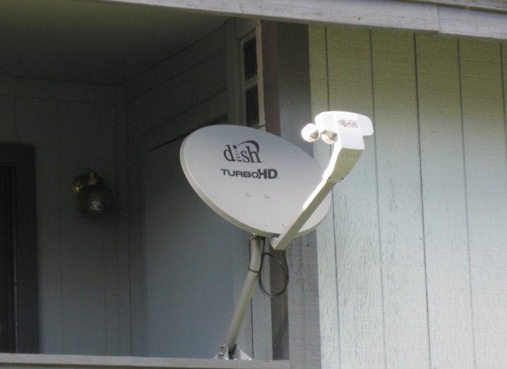 A satellite dish with the Dish Network logo on the front, connected to a building.