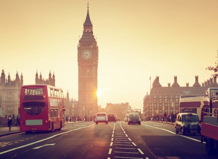 Westminster Bridge, with vehicles driving and Big Ben visible in the background, with the sun setting in the distance.