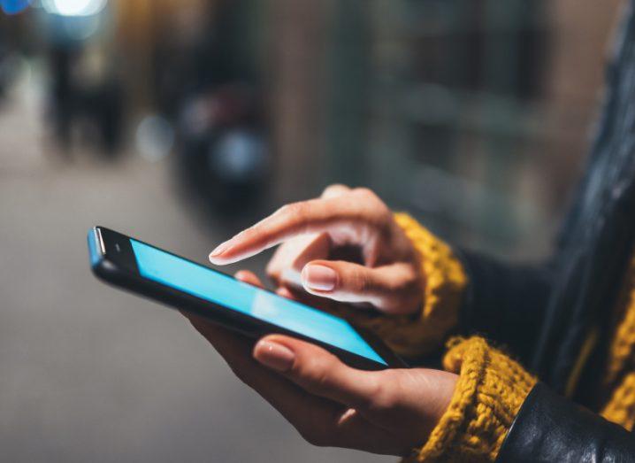 A mobile phone with a blue screen, being held in a person's hands with a city street in the background.