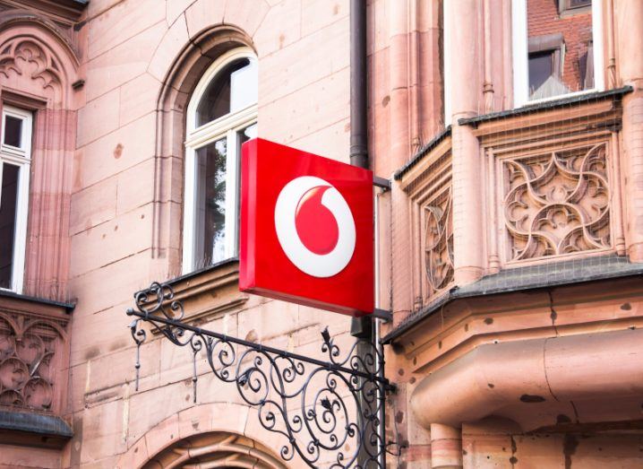 Vodafone logo hanging on the side of a building, with windows behind the sign.