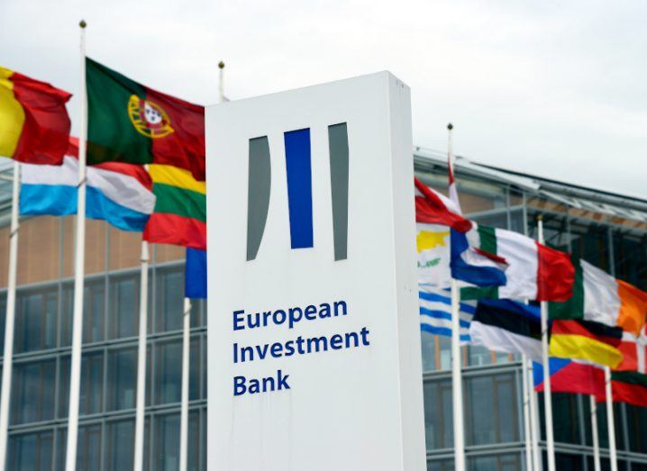 The European Investment Bank logo in front of multiple country flags, with a building in the background.