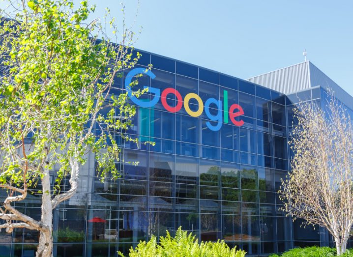 Google logo on a building, with trees in front and a blue sky above the building.