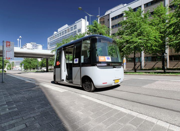 A self-driving shuttle on a quiet, tree-lined street in a built up urban area.