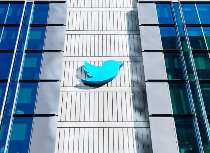 The Twitter logo on the side of a grey building, with windows on either side.