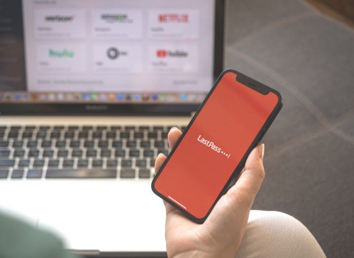 LastPass logo on a mobile phone, being held in a person's hands, with a laptop in the background.