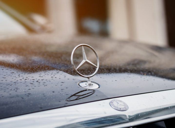 The Mercedes-Benz logo on the hood of a car with some rain droplets visible on the vehicle.