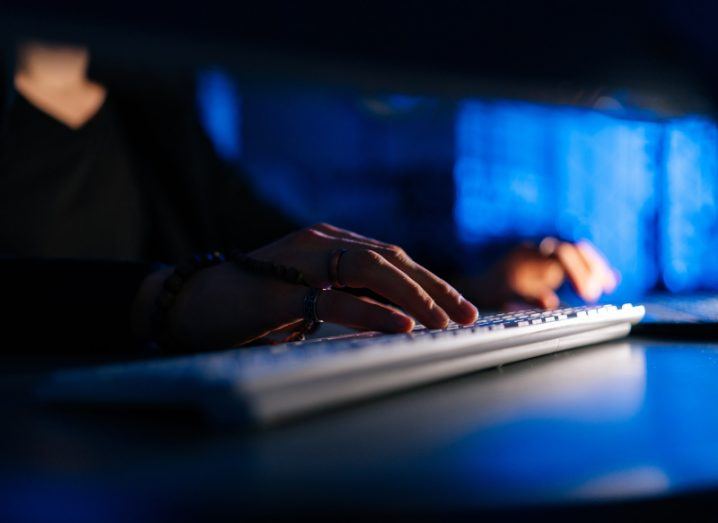 A person typing on a keyboard in a dark room, with blue lighting in the background.