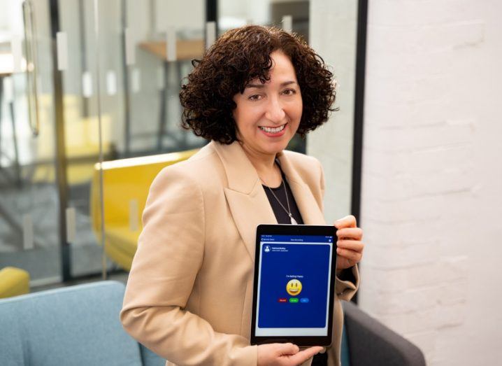 A woman smiles at the camera as she holds an iPad displaying the Empathic app. She is Dr Aviva Cohen, the CEO and co-founder of SeamlessCare.
