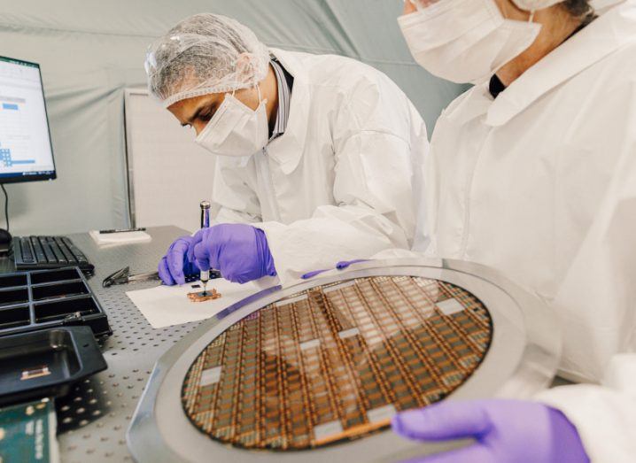 A clean room at Evonetix, where two workers in white uniforms and masks work with semiconductor chips.