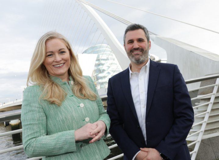 A woman and a man standing outside in front of a white modern looking bridge in Dublin.