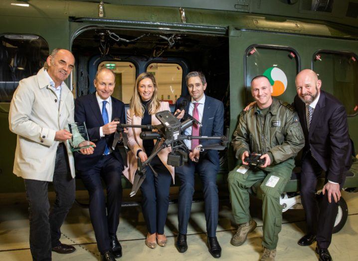 Ministers, academics and a member of the Defence Forces stand around a small remotely operated vehicle smiling.