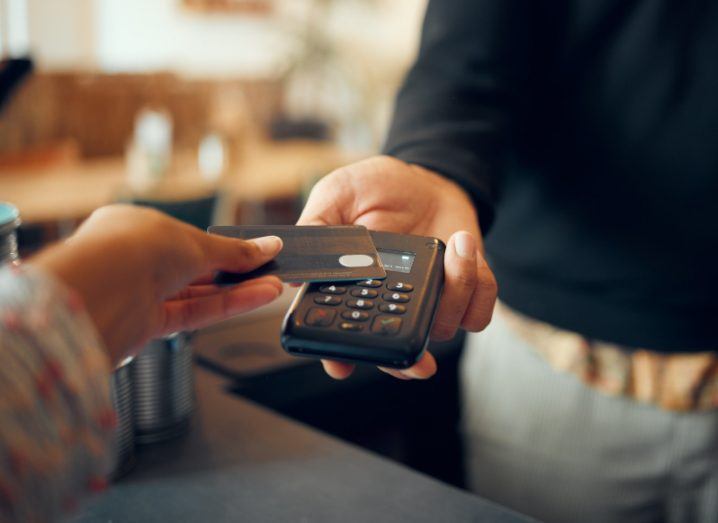 A person holding a bank card over a reader machine making a contactless payment.