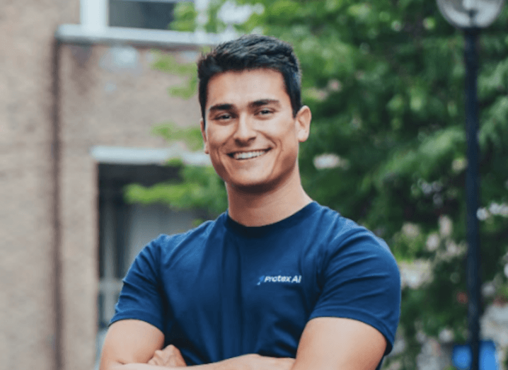 Headshot of Protex AI CEO Dan Hobbs wearing a blue t-shirt and posing outdoors with his arms folded over his chest.