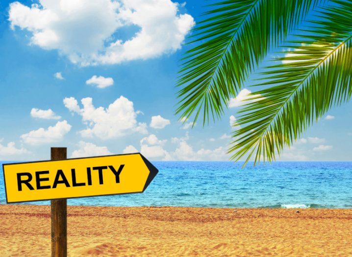 Tropical beach with blue sea and sky and palm fronds and a sign saying REALITY