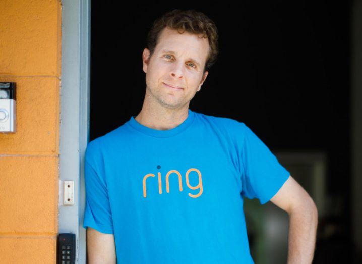 Ring founder Jamie Siminoff standing in front of a doorway wearing a blue t-shirt with the Ring logo on it.