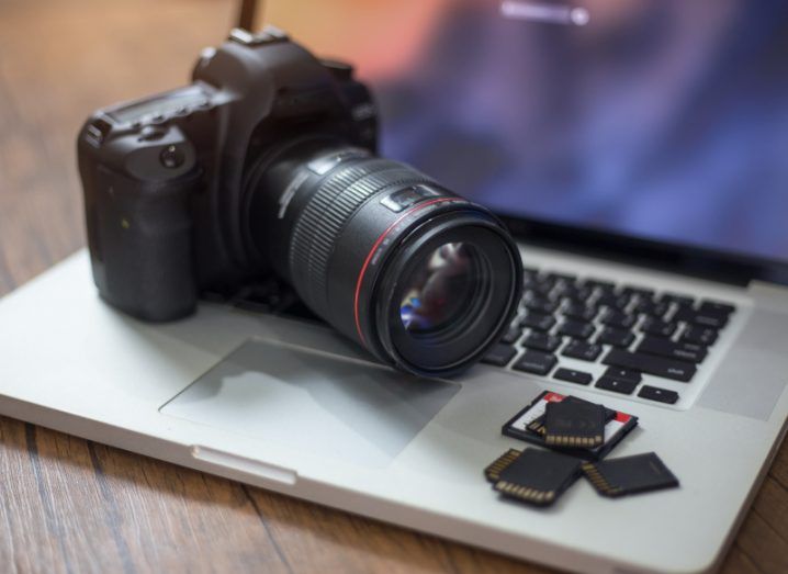 A camera lying on top of a grey laptop, with three memory cards in front of the camera.
