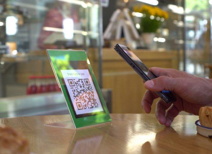 A QR scan code on a wooden table, with a person using their mobile phone to scan it.