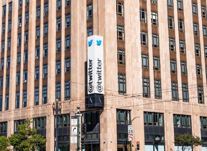 The Twitter logo on a white sign, hanging on the side of a brown building.