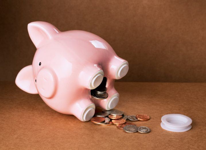 A piggy bank on it's side, with coins spilling out onto a brown surface.