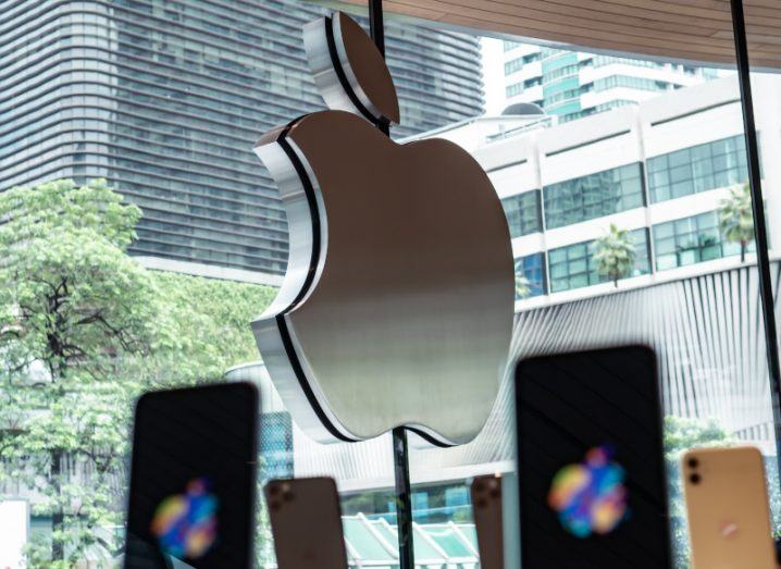 The Apple logo on the window of a store, with smartphones visible on displays.