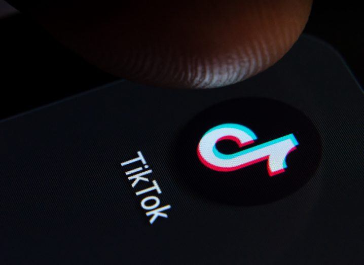 The TikTok logo on a screen, about to be touched by a person's finger.