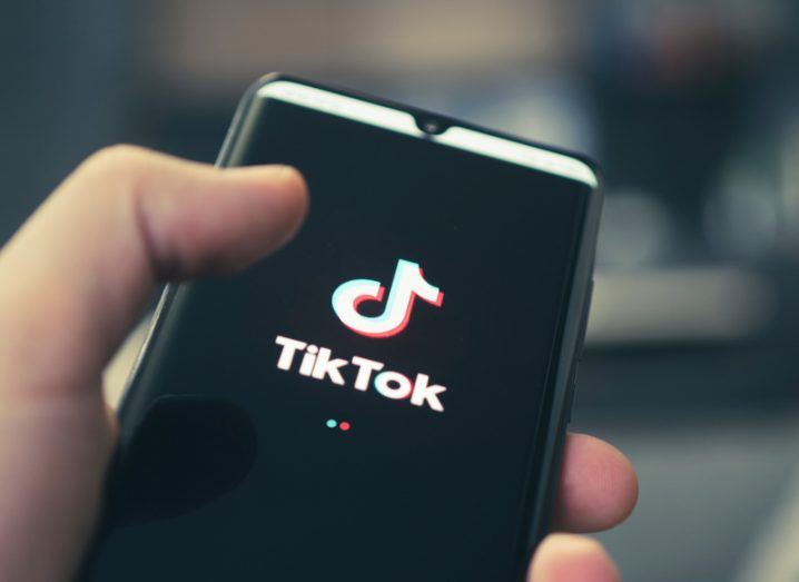 The TikTok logo on a mobile phone, held in a person's hand.