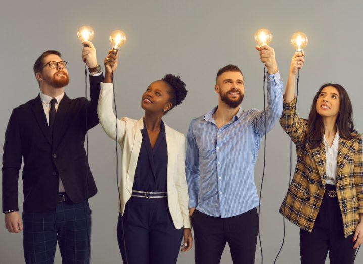 People standing in a row together holding up light bulbs.