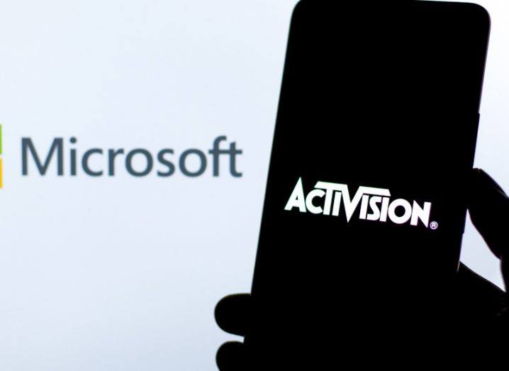 The Activision logo on a mobile phone screen, held in a person's hand with the Microsoft name on a white background behind the phone.