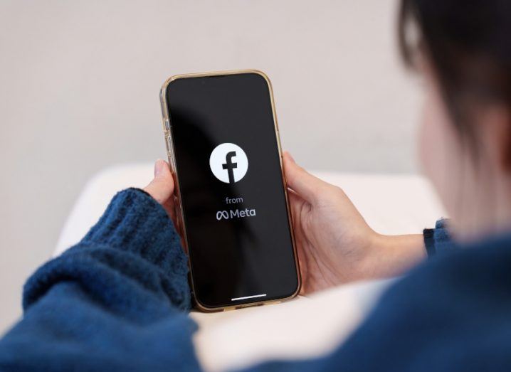 The Facebook and Meta logo on a smartphone screen, held in a person's hands.