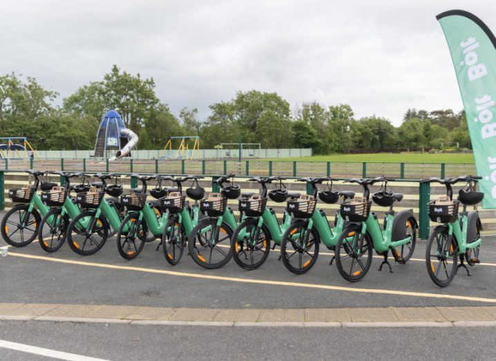 A row of Bolt e-bikes in front of a park, next to a green flag with the Bolt logo on it.