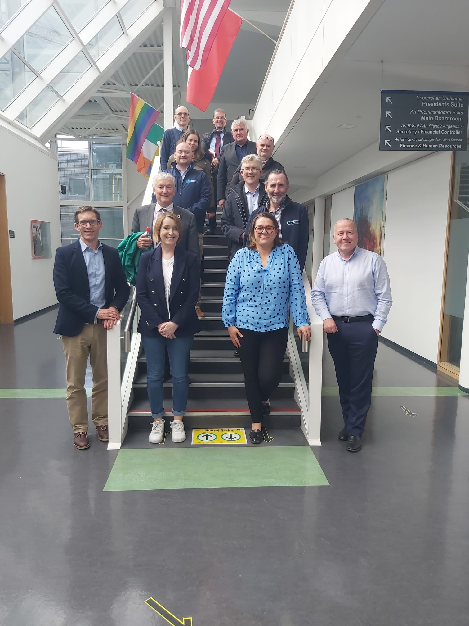 Members of the ATU engineering consortium group standing together on a stairway in the lobby area of a building lit by natural light.