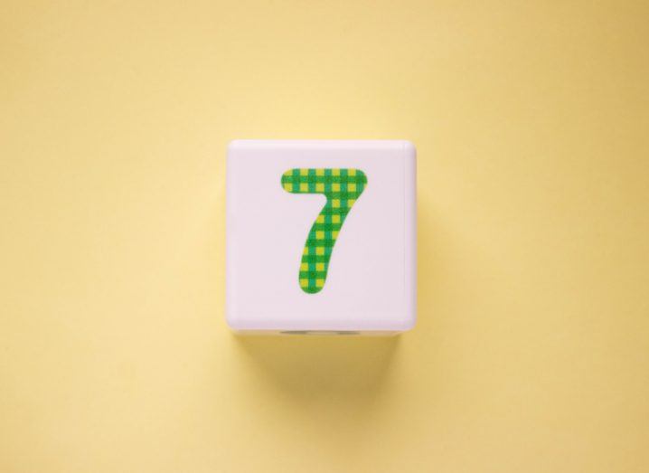 Close-up photo of a white plastic cube with a green number 7 on a yellow background.