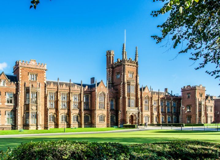 Queen's University Belfast with a grass lawn, tree branches and a hedge in sunset light.