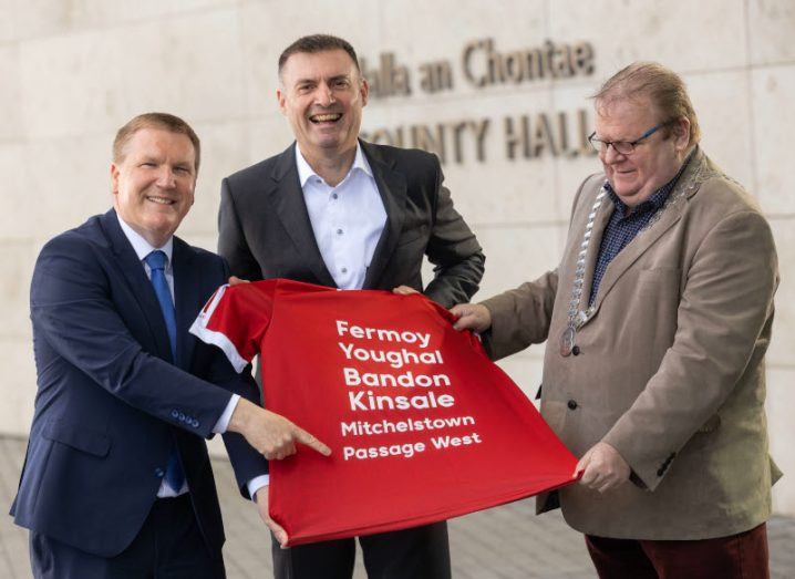 Three men hold a red banner that reads the names of the six Cork towns getting connected to the Siro fibre network.