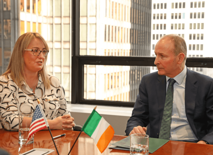 FlowForma CEO Olivia Bushe seated at a table in conversation with Micheál Martin. The Irish tricolour and the US flag can be seen in the foreground.