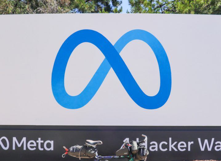 The Meta company logo on a white signpost, with a bike below it and trees behind it.