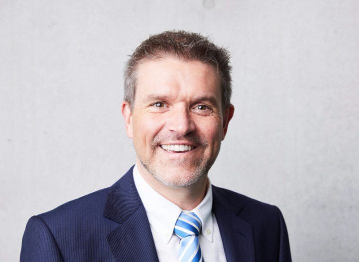 Headshot of a man wearing a suit and tie with a grey wall background.