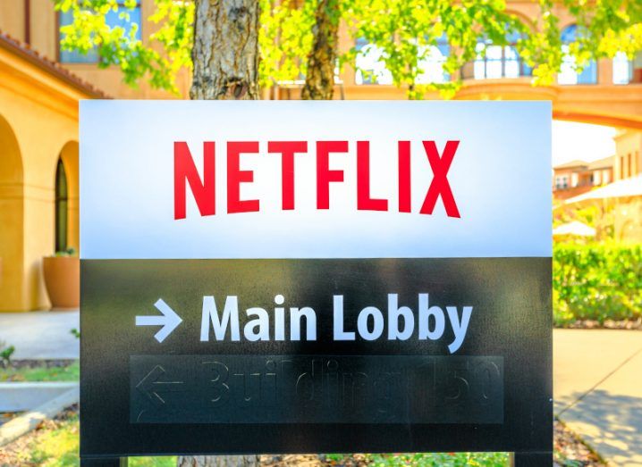 The Netflix logo on a sign in front of a couple of trees and buildings. The sign also has an arrow pointing toward the "main lobby".