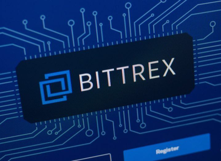 The Bittrex logo on a screen with blue lines moving out from all directions around it. A "register" button is visible on the bottom of the image.
