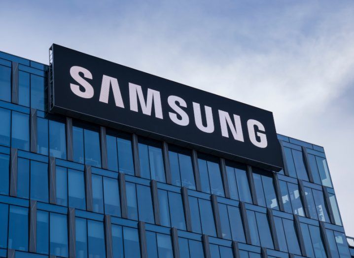 The Samsung logo on the top of a tall building with a grey sky above it.