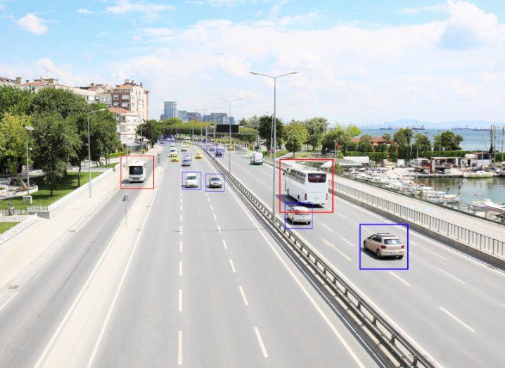 A view of a motorway with cars and trucks driving on it with some vehicles framed on a screen or with machine learning tech.