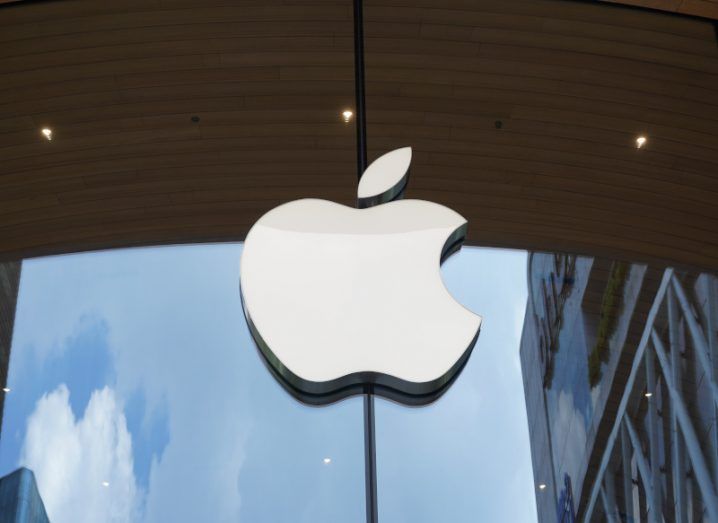 The Apple company logo on the front of a window, with the sky and a building being reflected on the glass.
