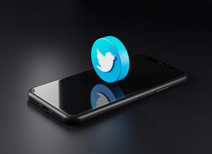 A 3D Twitter logo on top of a smartphone screen, in a dark background.