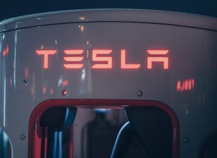The Tesla logo on the front of a white charging station at night.